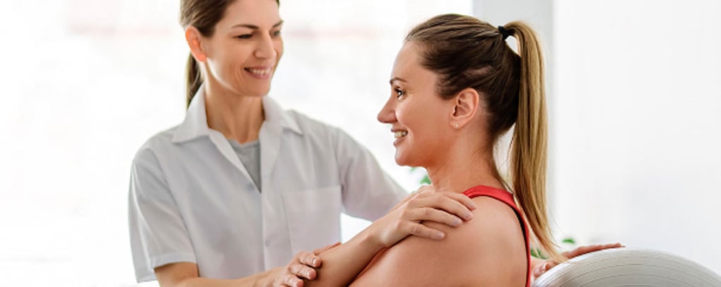 therapist helping patient on exercise ball