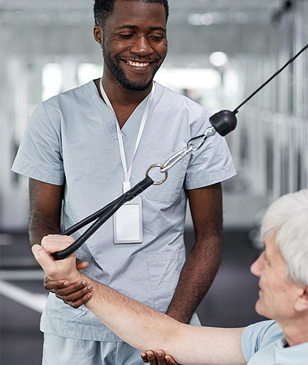 physical therapist assists elderly man on gym equipment